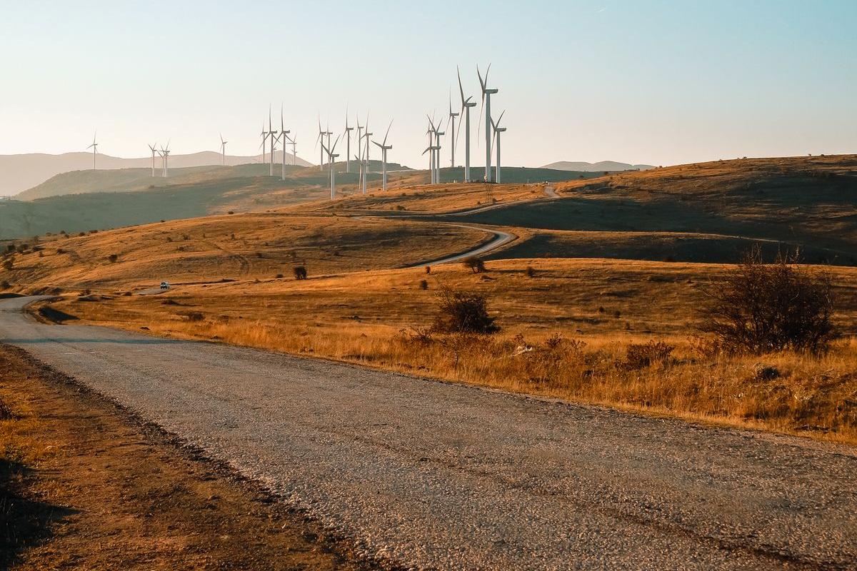 夕方の丘陵地帯に並ぶ風力発電の風車と一本道。地域で発電された電気のイメージ