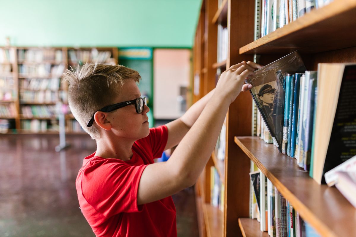 学校の図書室で本棚から本を取る子ども
