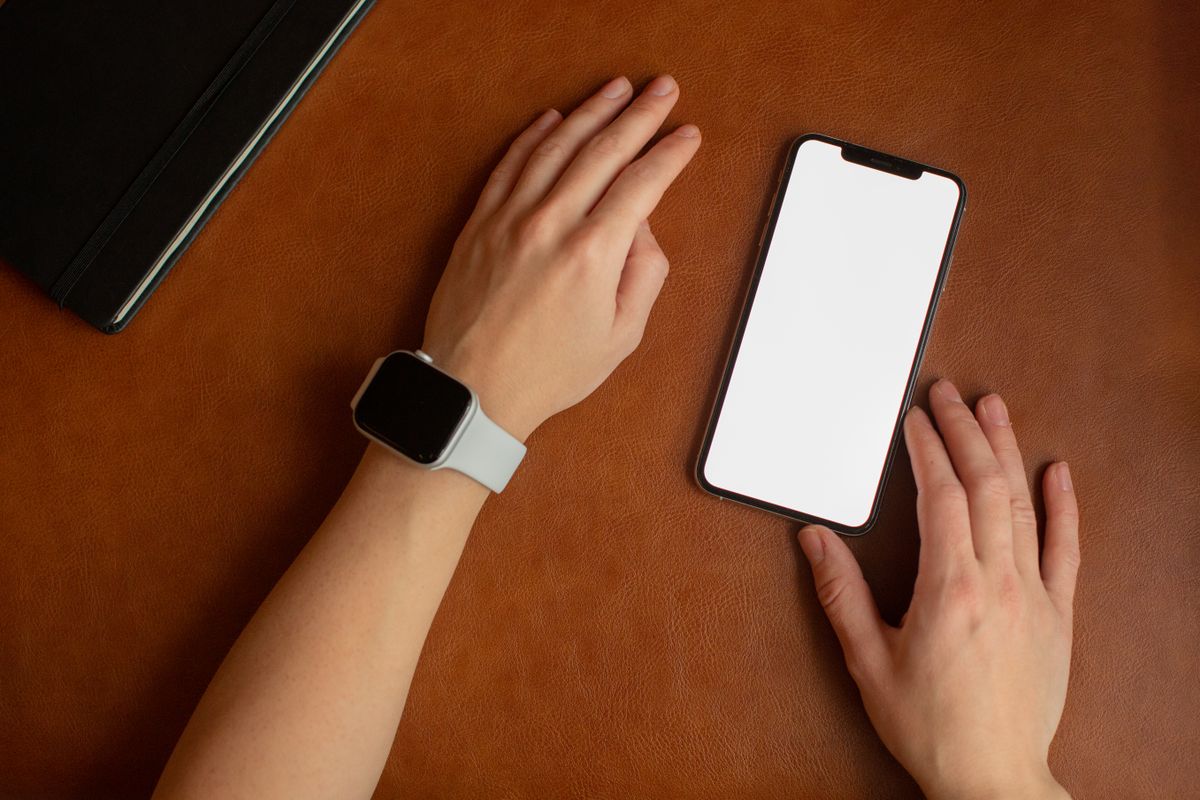スマートウォッチを着けた手とスマートフォンが机の上に並んでいる様子
