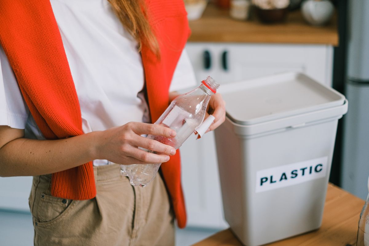 使用済みのペットボトルを手に持ち、プラスチック用の回収ボックスに入れようとする人