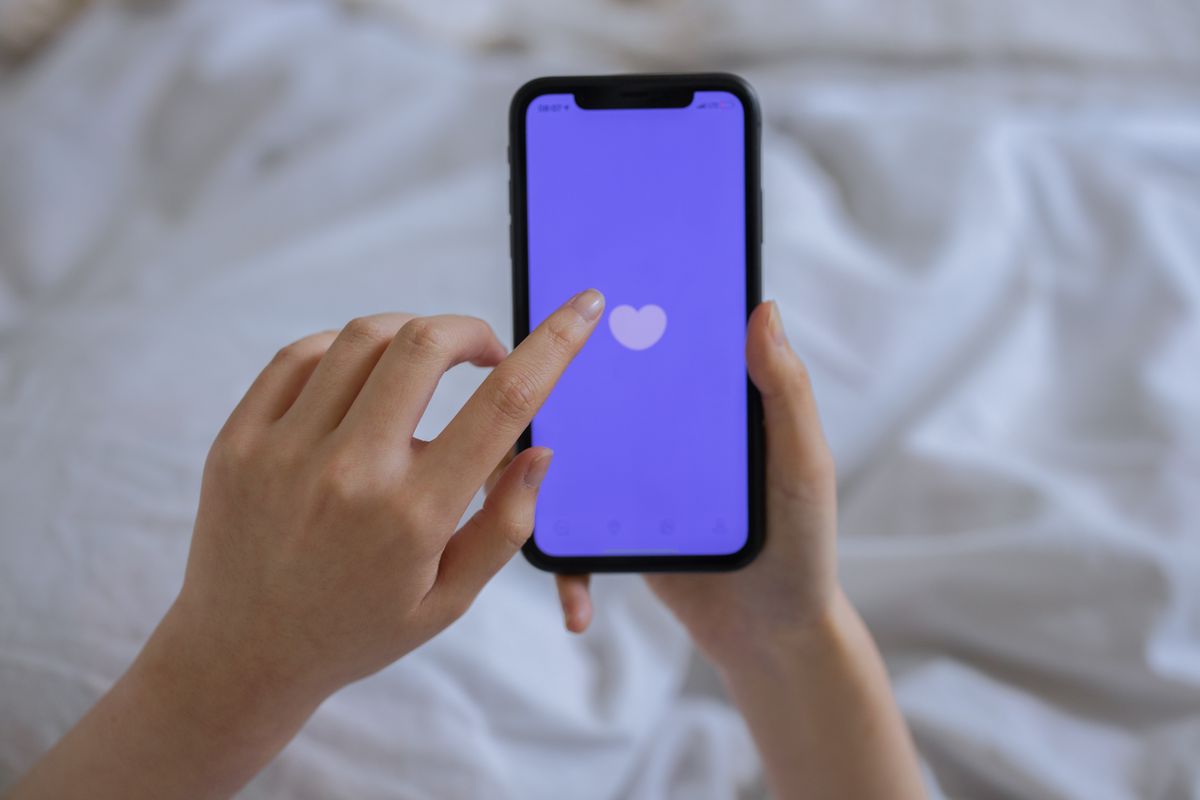 スマートフォンの画面に表示されたハートを指でタッチする手元、アンケートや応援の操作のイメージ