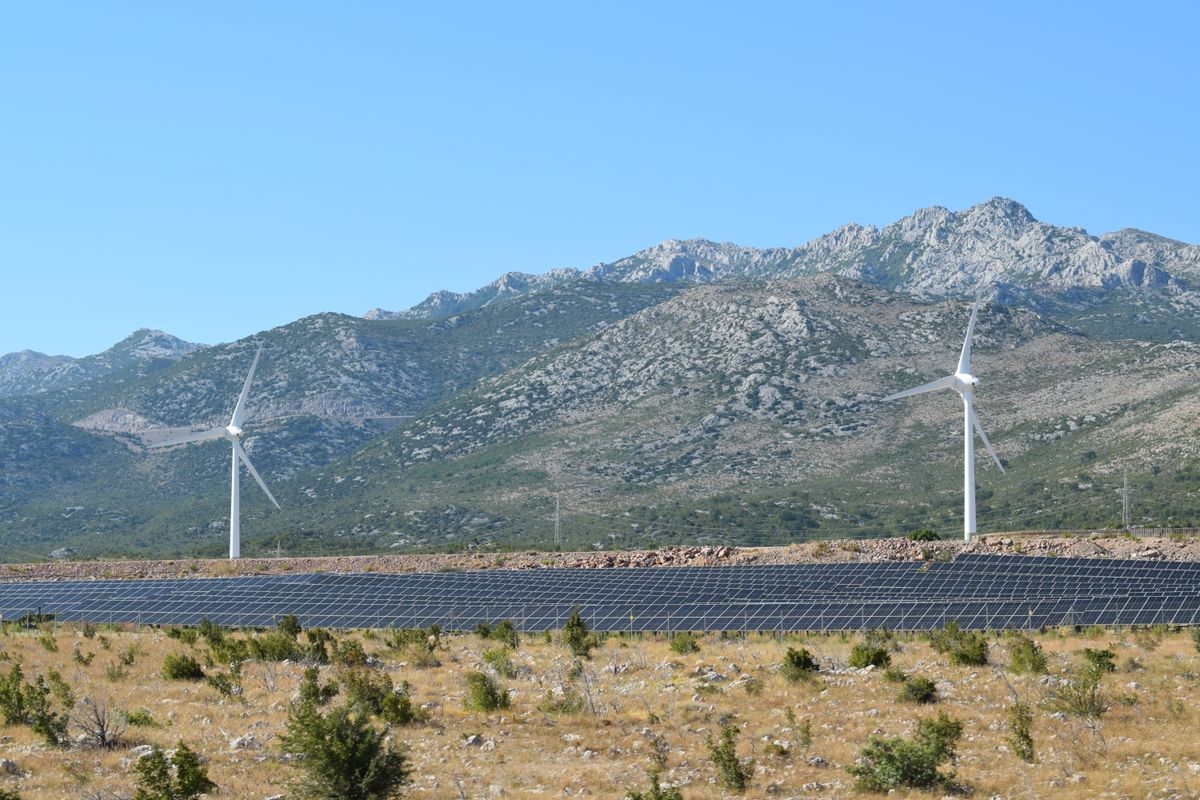 山を背景に風力発電の風車と太陽光パネルが並ぶ再生可能エネルギーの発電所