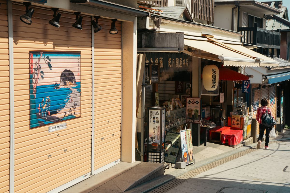 神奈川県の商店街で、シャッターの絵や店先の看板が並ぶ路地を歩く人