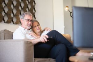ソファに並んでテレビを見る高齢の夫婦。まごチャンネルで孫の動画を見る場面のイメージ