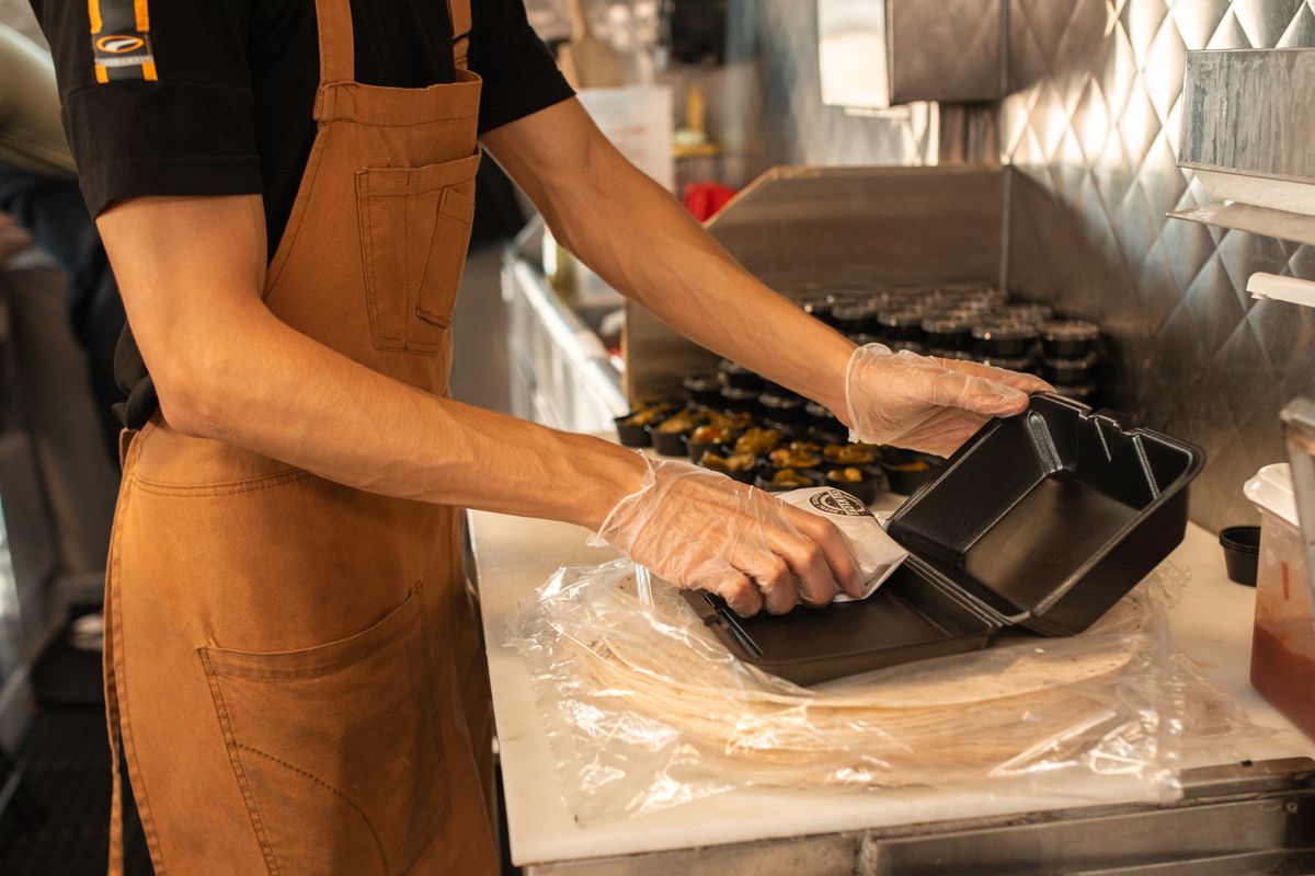厨房で持ち帰り用の容器に料理を詰める店員