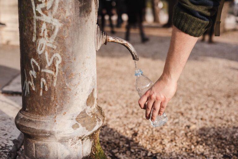 公園の古い水飲み場の蛇口から、手に持ったペットボトルに水を入れている様子