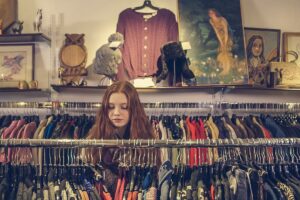 ハンガーラックの服を選ぶ女性。アウトレット通販で服を探す場面のイメージ
