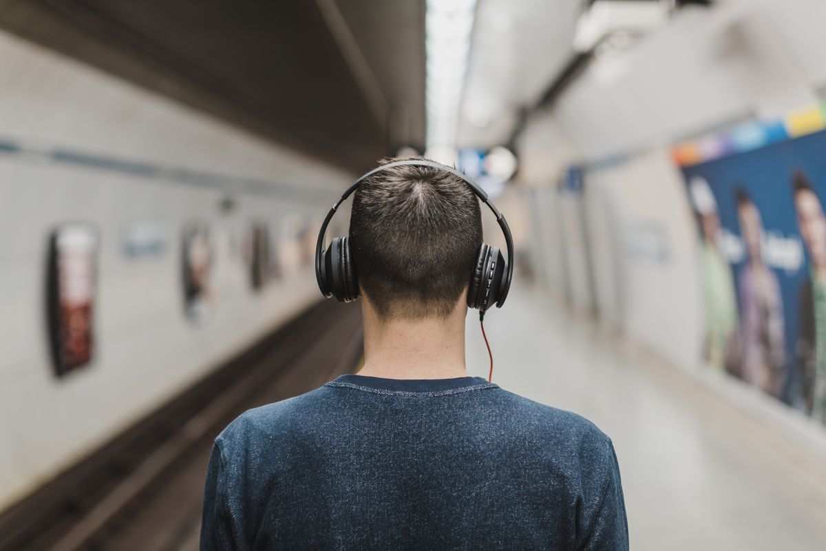 ヘッドホンで音楽を聴きながら駅のホームを歩く人