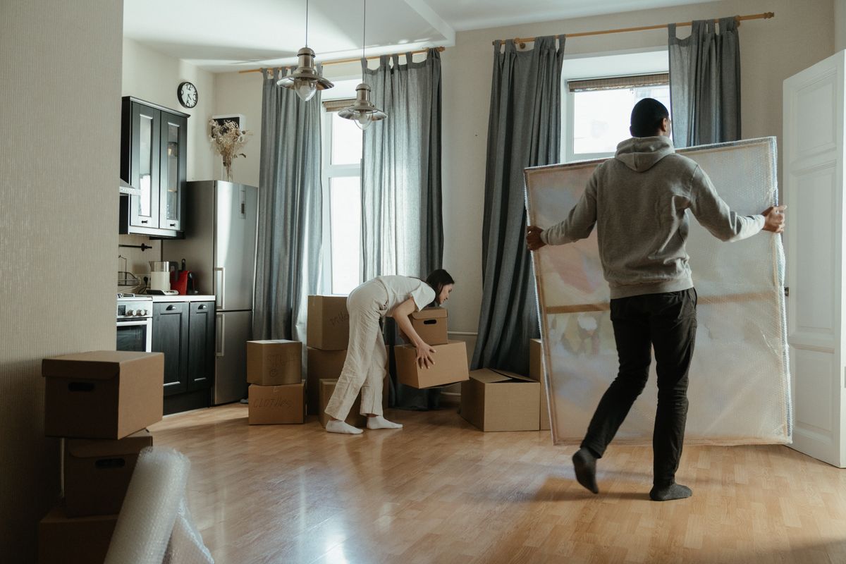 段ボール箱が積まれた部屋で荷物を運ぶ二人