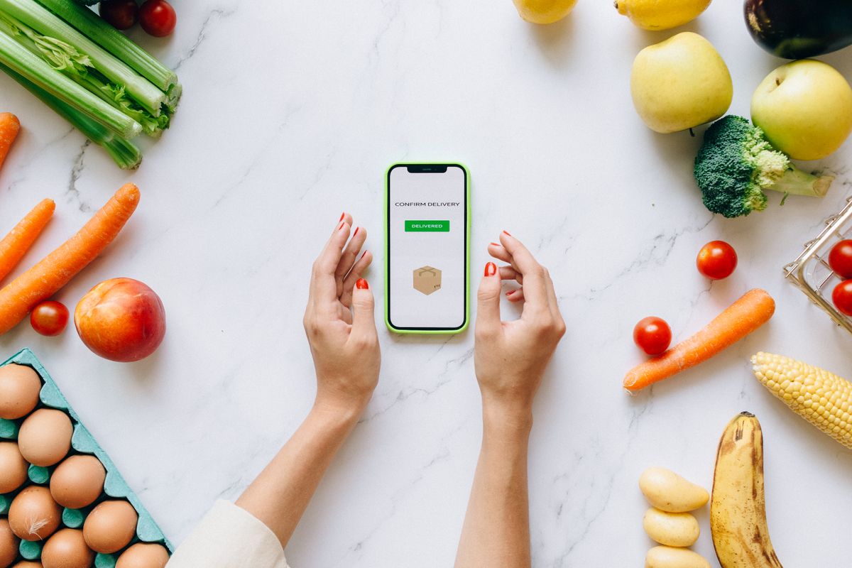 スマートフォンのアプリ画面と野菜や果物が並ぶ食材のイメージ