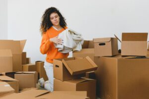 段ボール箱に囲まれて衣類を整理する女性。宅配買取の準備のイメージ
