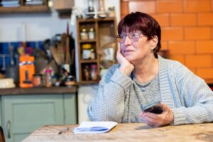スマートフォンを手にテーブルで物思いにふける高齢の女性
