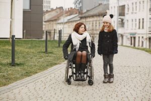 石畳の道を車いすで進む女性と、寄り添って歩く女の子